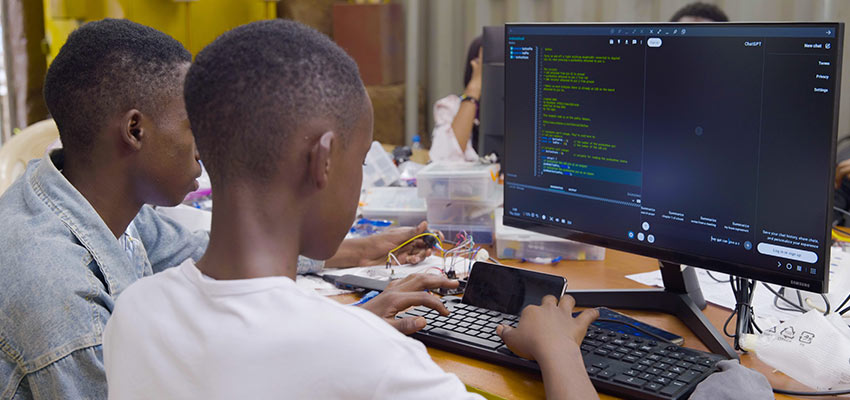 ICT workshop youth participants in Tanzania learning how to code using a smartphone (Samsung DEX) and AI Chatbots.